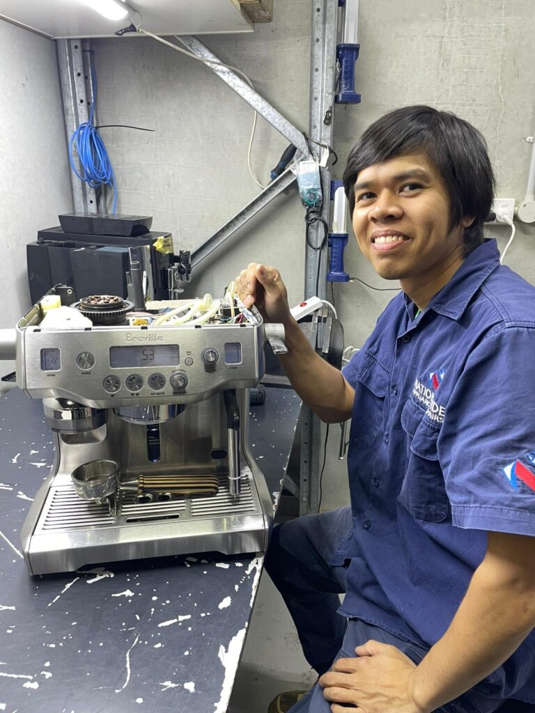 NAR technician posing in front of a partly-disassembled Breville-branded coffee machine, with the number “53” displaying on the screen.