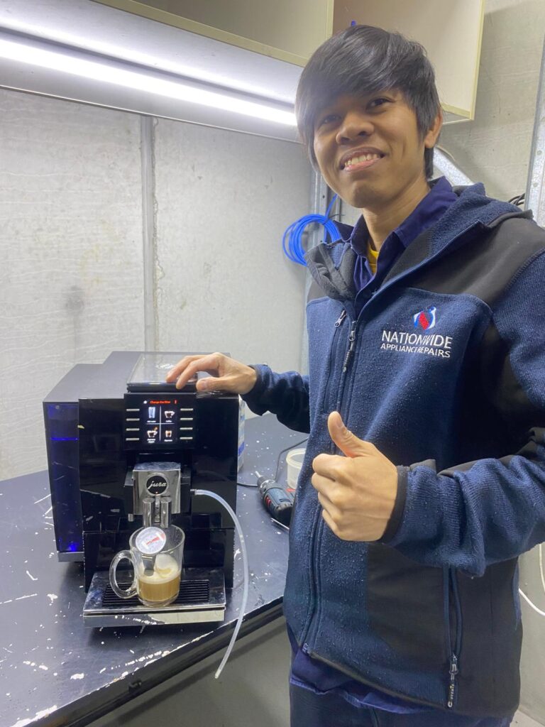 NAR technician posing in front of a repaired Jura machine, with a freshly-brewed cup of coffee in the tray.