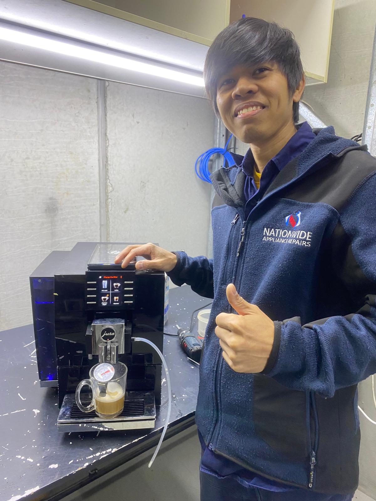 NAR technician posing in front of a repaired Jura machine, with a freshly-brewed cup of coffee in the tray. NAR technician posing in front of a repaired Jura machine, with a freshly-brewed cup of coffee in the tray.