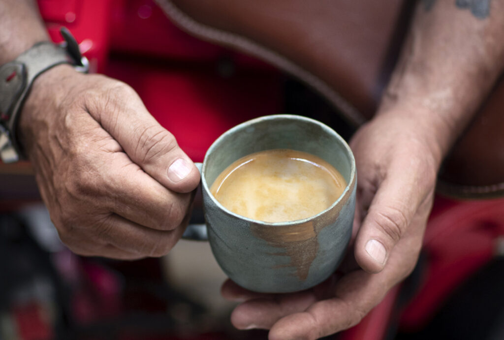 Person holding a cup of milky coffee in a teal ceramic cup.