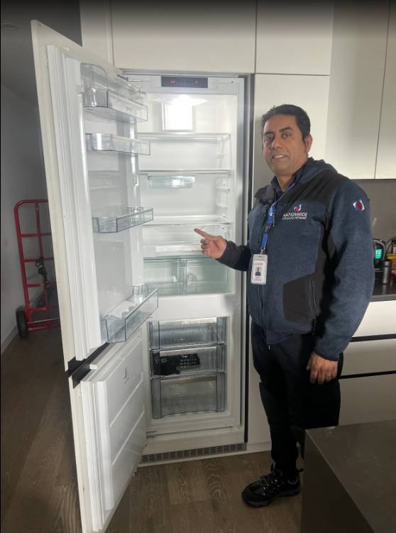 NAR technician posing in front of an emptied-out fridge that’s recently been repaired in a customer’s residence.