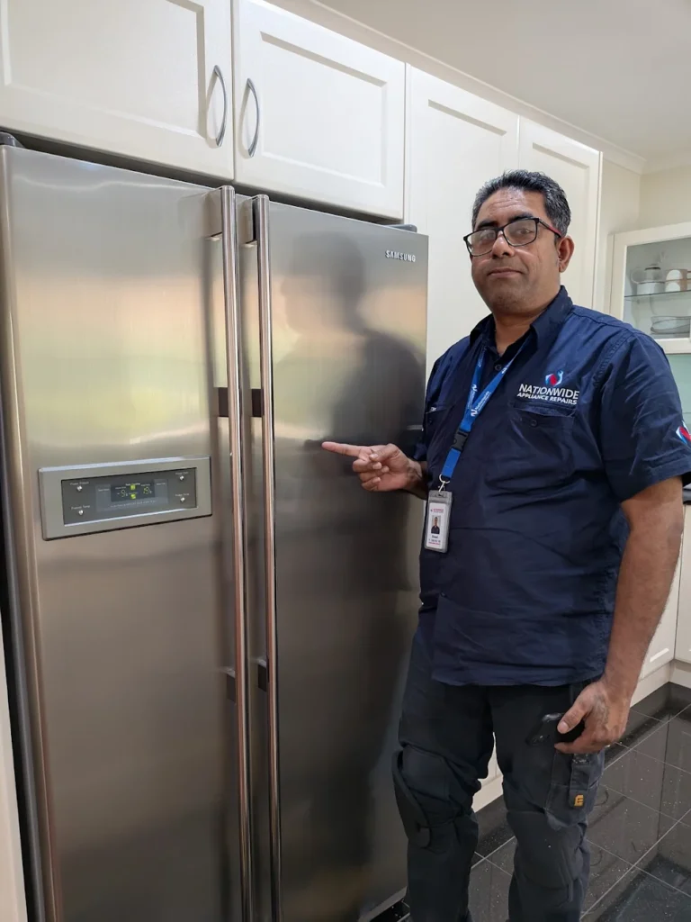NAR technician standing, posing, and gesturing at a Samsung fridge that’s recently been repaired in a customer’s residence.
