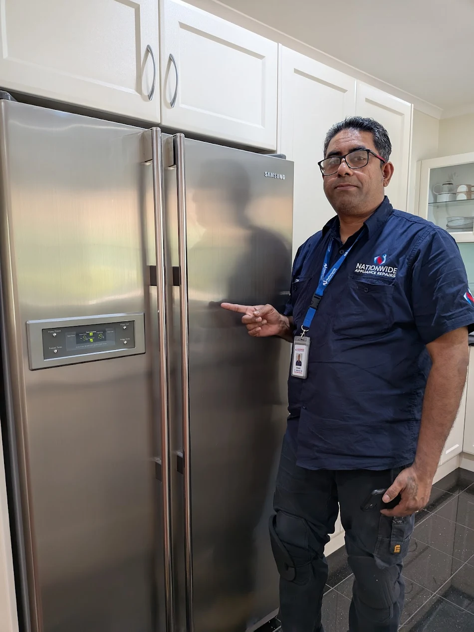 NAR technician standing, posing, and gesturing at a Samsung fridge that’s recently been repaired in a customer’s residence. NAR technician standing, posing, and gesturing at a Samsung fridge that’s recently been repaired in a customer’s residence.