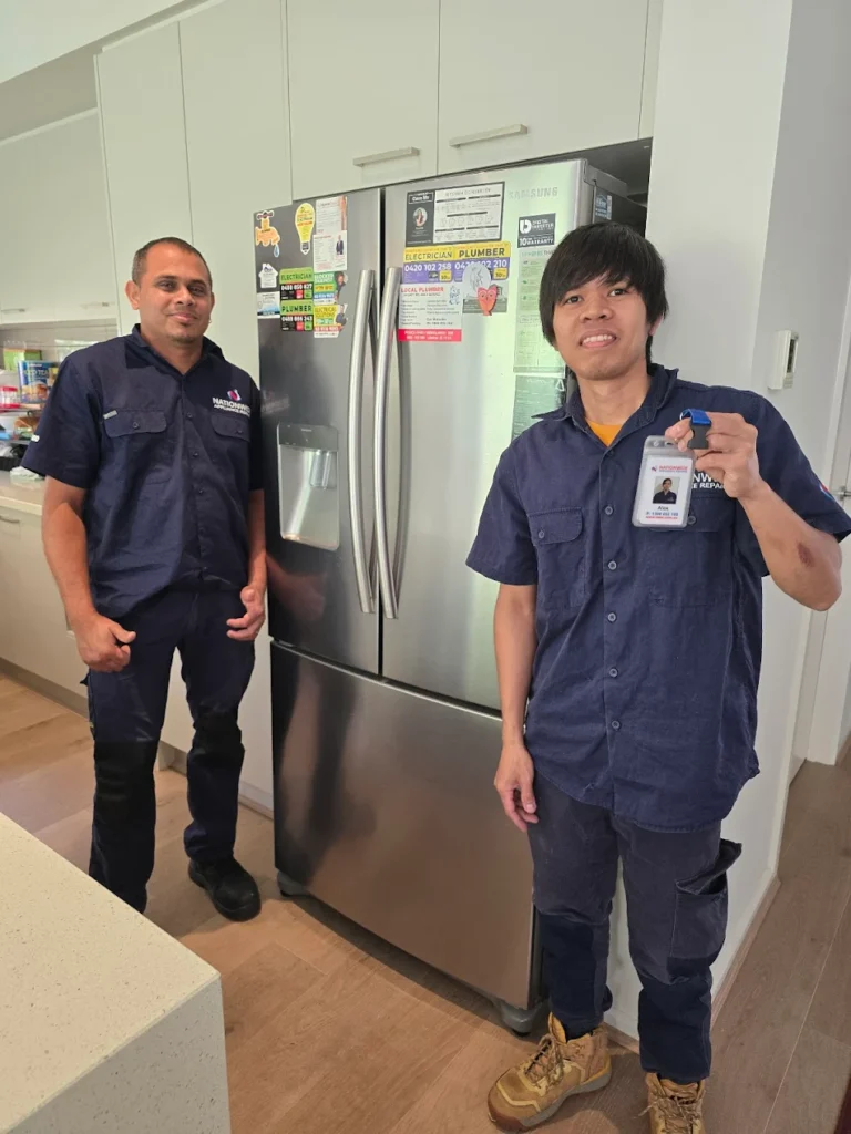 Two NAR technicians standing in front of a Samsung fridge, one holding his ID badge, in a customer’s kitchen.