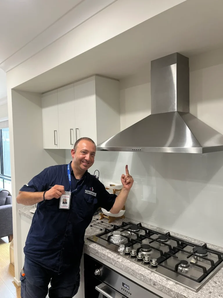 A NAR technician posing in front of a metallic rangehood and stove range.