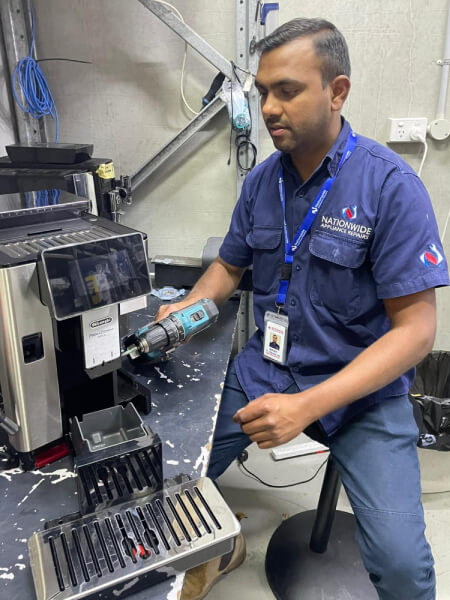 NAR technician using a power tool to repair a Delonghi-branded coffee machine.