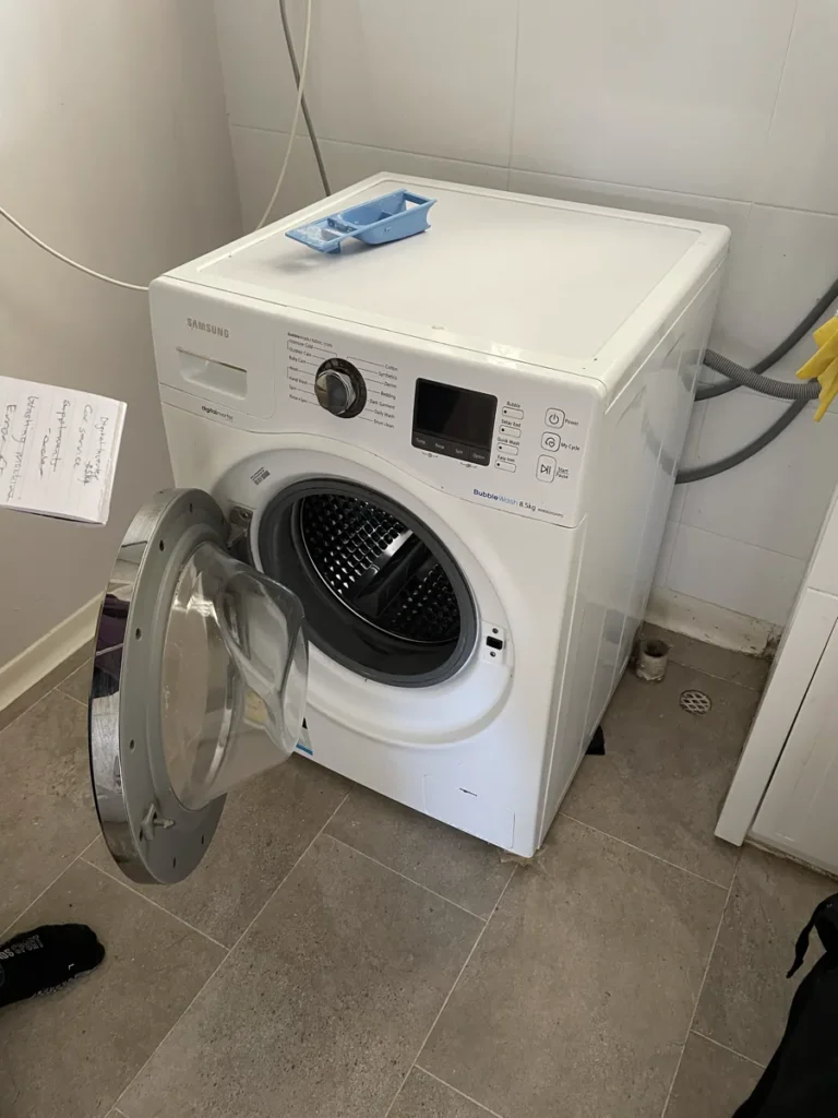 A front-loading Samsung washing machine in a client’s home, with the door opened.