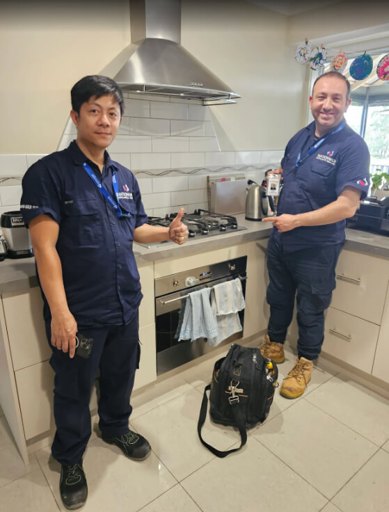 Two technicians giving thumb ups in front of a rangehood in a NAR client’s home.