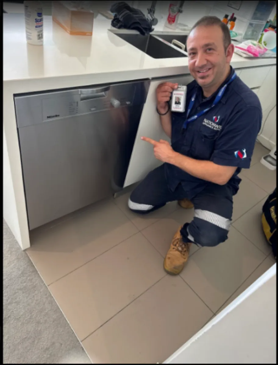 NAR technician holding his badge and pointing at a Miele dishwasher.