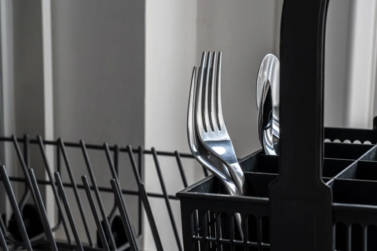 Utensils sitting in black tray of a warewasher.